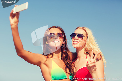 Image of two smiling women making selfie on beach