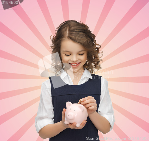 Image of happy girl putting coin into piggy bank