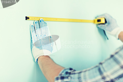 Image of closeup of male in gloves measuring wall with tape