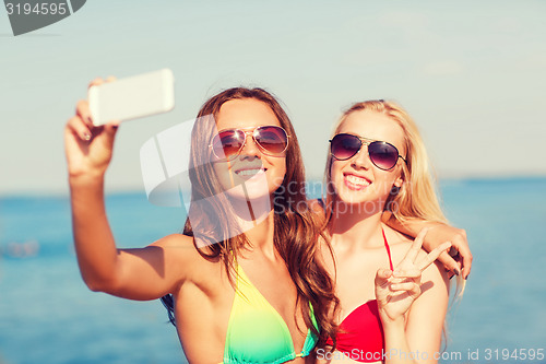 Image of two smiling women making selfie on beach