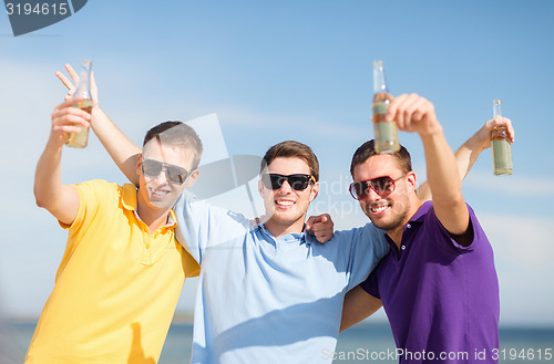 Image of happy friends with beer bottles on beach