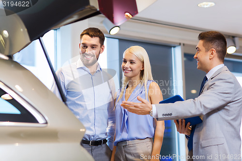 Image of happy couple with car dealer in auto show or salon