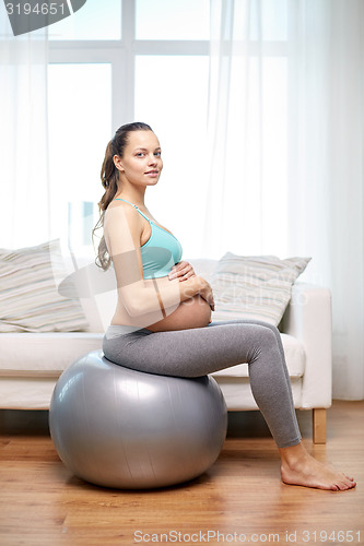 Image of happy pregnant woman exercising on fitball at home