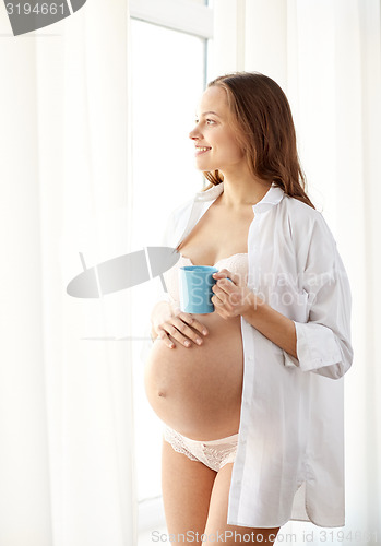 Image of happy pregnant woman with cup drinking tea at home