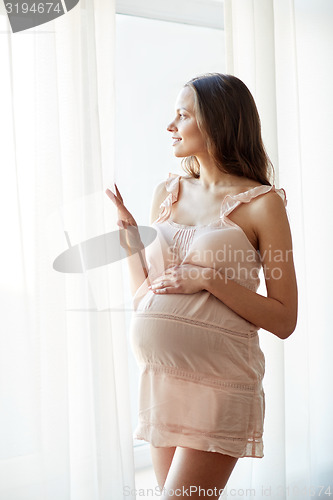 Image of happy pregnant woman near window at home