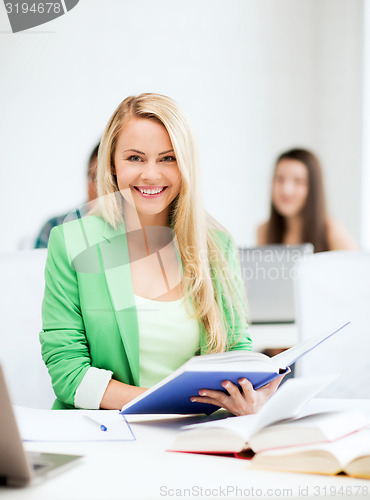 Image of smiling young woman reading book at school