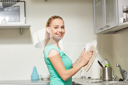 Image of happy woman wiping dishes at home kitchen