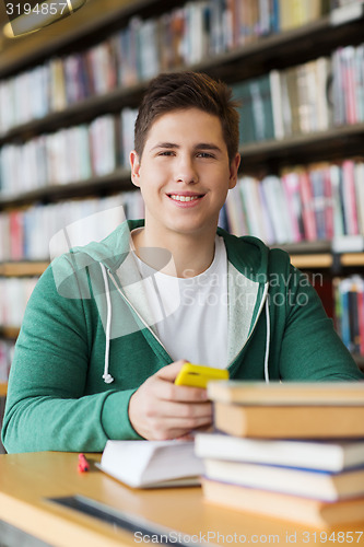 Image of male student with smartphone and books in library