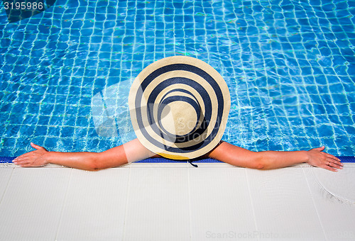 Image of Woman in straw hat relaxing swimming pool