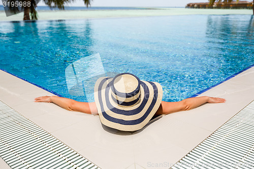 Image of Woman in straw hat relaxing swimming pool