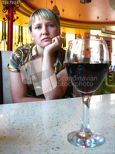 Image of glass of red wine on the table and a lonely girl