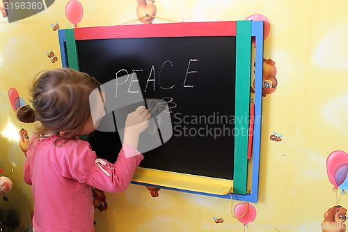 Image of girl writes on a blackboard a word the peace