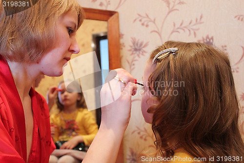 Image of mother makes up daughter's face before a mirror