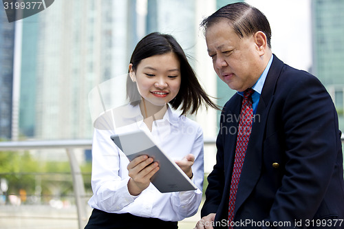 Image of Asian businessman and young female executive looking at tablet