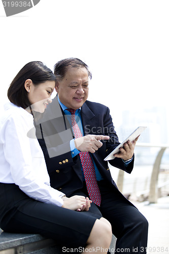 Image of Asian businessman and young female executive looking at tablet