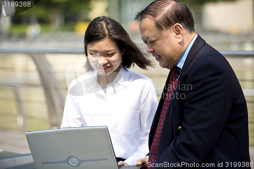 Image of Asian businessman and young female executive looking at laptop