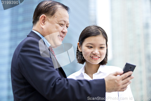 Image of Asian businessman and young female executive looking at smart phone