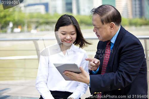 Image of Asian businessman and young female executive looking at tablet