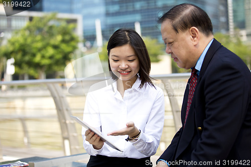 Image of Asian businessman and young female executive looking at tablet