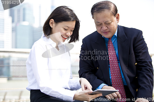 Image of Asian businessman and young female executive looking at tablet