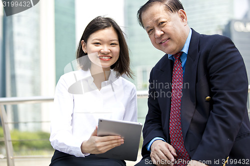 Image of Asian businessman and young female executive looking at tablet