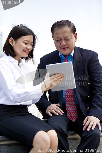 Image of Asian businessman and young female executive looking at tablet