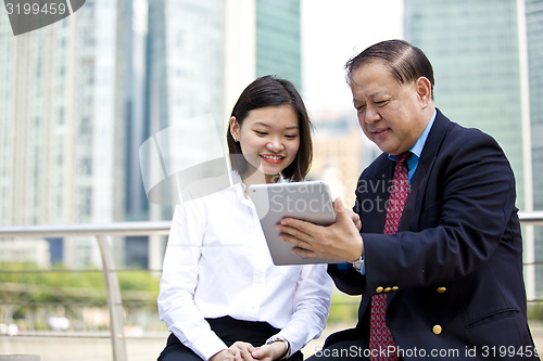 Image of Asian businessman and young female executive looking at tablet