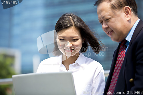 Image of Asian businessman and young female executive looking at laptop