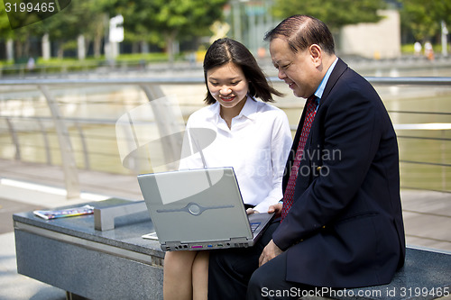 Image of Asian businessman and young female executive looking at laptop