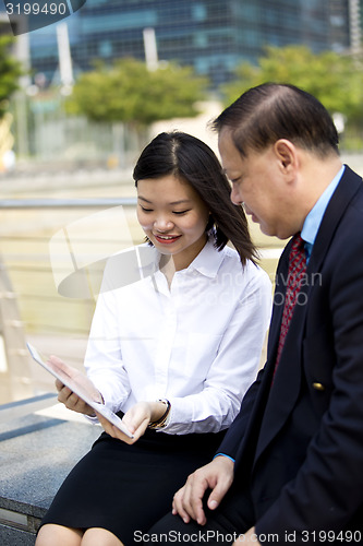 Image of Asian businessman & young female executive looking at tablet