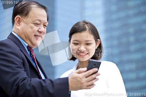 Image of Asian businessman & young female executive looking at smart phone