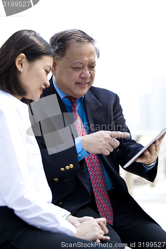 Image of Asian businessman & young female executive looking at tablet