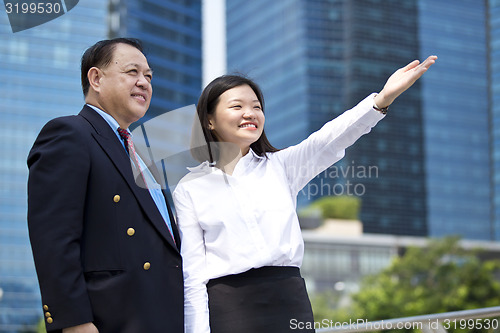 Image of Asian businessman & young female executive pointing at a direction