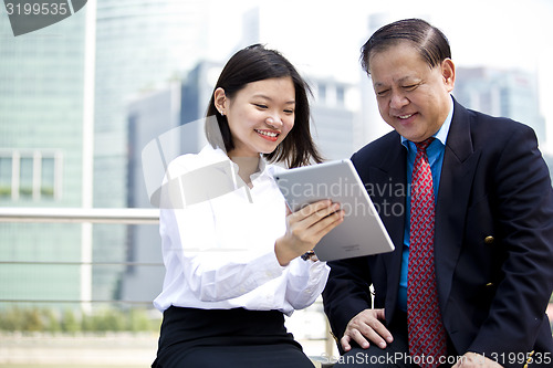 Image of Asian businessman & young female executive looking at tablet