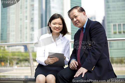 Image of Asian businessman & young female executive looking at tablet