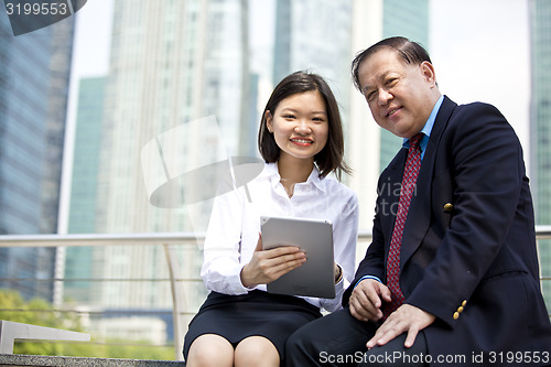Image of Asian businessman and young female executive using tablet