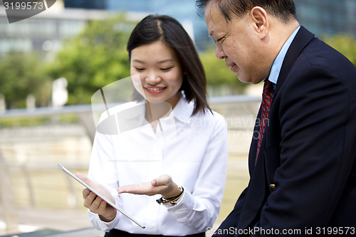 Image of Asian businessman and young female executive using tablet