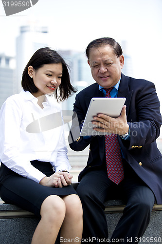 Image of Asian businessman and young female executive using tablet