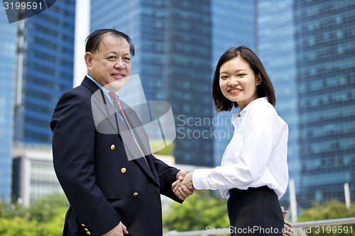 Image of Asian businessman and young female executive shaking hands