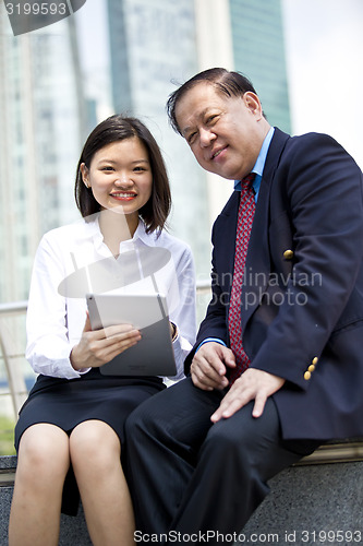 Image of Asian businessman and young female executive using tablet