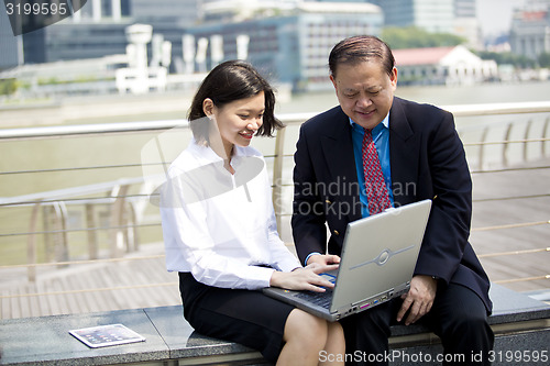 Image of Asian businessman and young female executive using laptop