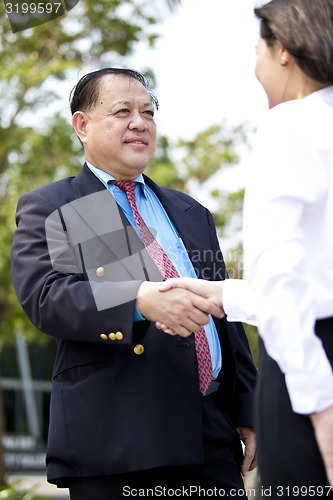 Image of Asian businessman and young female executive shaking hands
