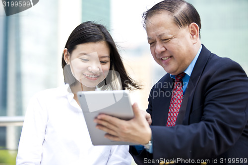 Image of Asian businessman and young female executive using tablet