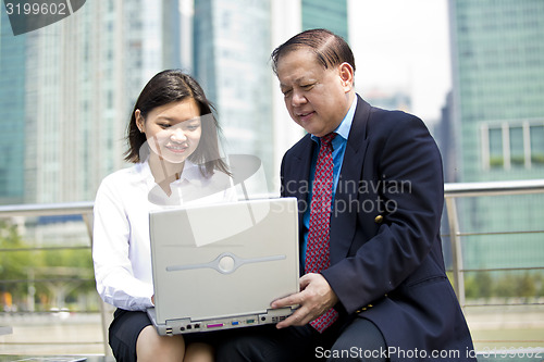 Image of Asian businessman and young female executive using laptop