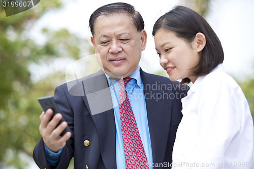 Image of Asian businessman and young female looking at smart phone