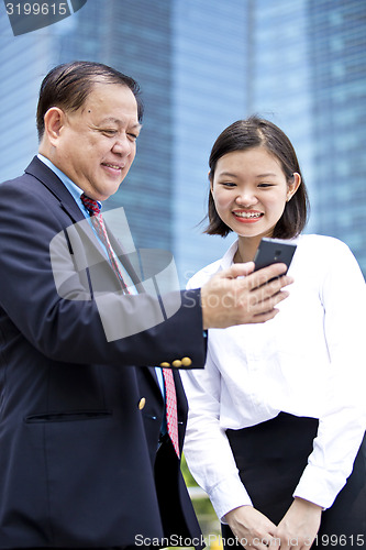 Image of Asian businessman and young female executive looking at smart phone