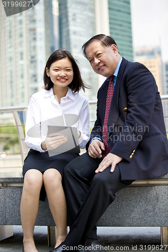 Image of Asian businessman and young female executive using tablet