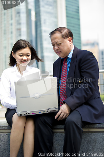Image of Asian businessman and young female executive using laptop