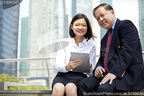 Image of Asian businessman and young female executive using tablet