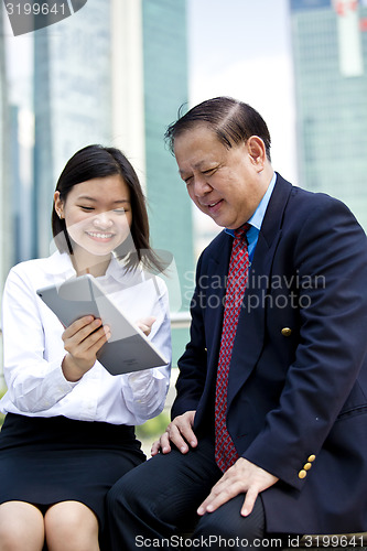 Image of Asian businessman and young female executive using tablet